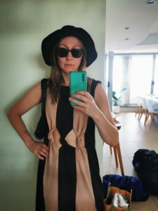 Lucy Baker in a beige and black dress and a black sun hat and sunglasses
